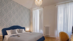 Ein Schlafzimmer mit einem großen Bett, einem Nachttisch, einem Sessel, einer Heizung und einem Fenster mit Vorhängen.