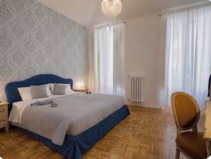 A bedroom with a large bed, a nightstand, a chair, a radiator, and a window with curtains. - Vrbo Property (roma)
