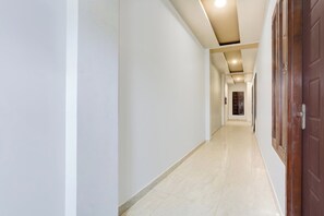 Un pasillo largo y estrecho con paredes blancas y suelo de baldosas, que conduce a una puerta al final.