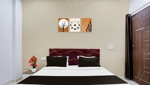 A hotel room with a bed, a nightstand with a vase of flowers, and three wall art pieces above the bed. - OYO Hotel O Bareilly Near Bus Stand (Bareilly)