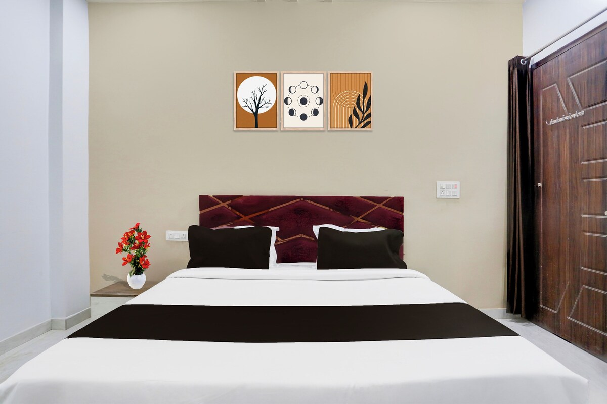 A hotel room with a bed, a nightstand with a vase of flowers, and three wall art pieces above the bed.