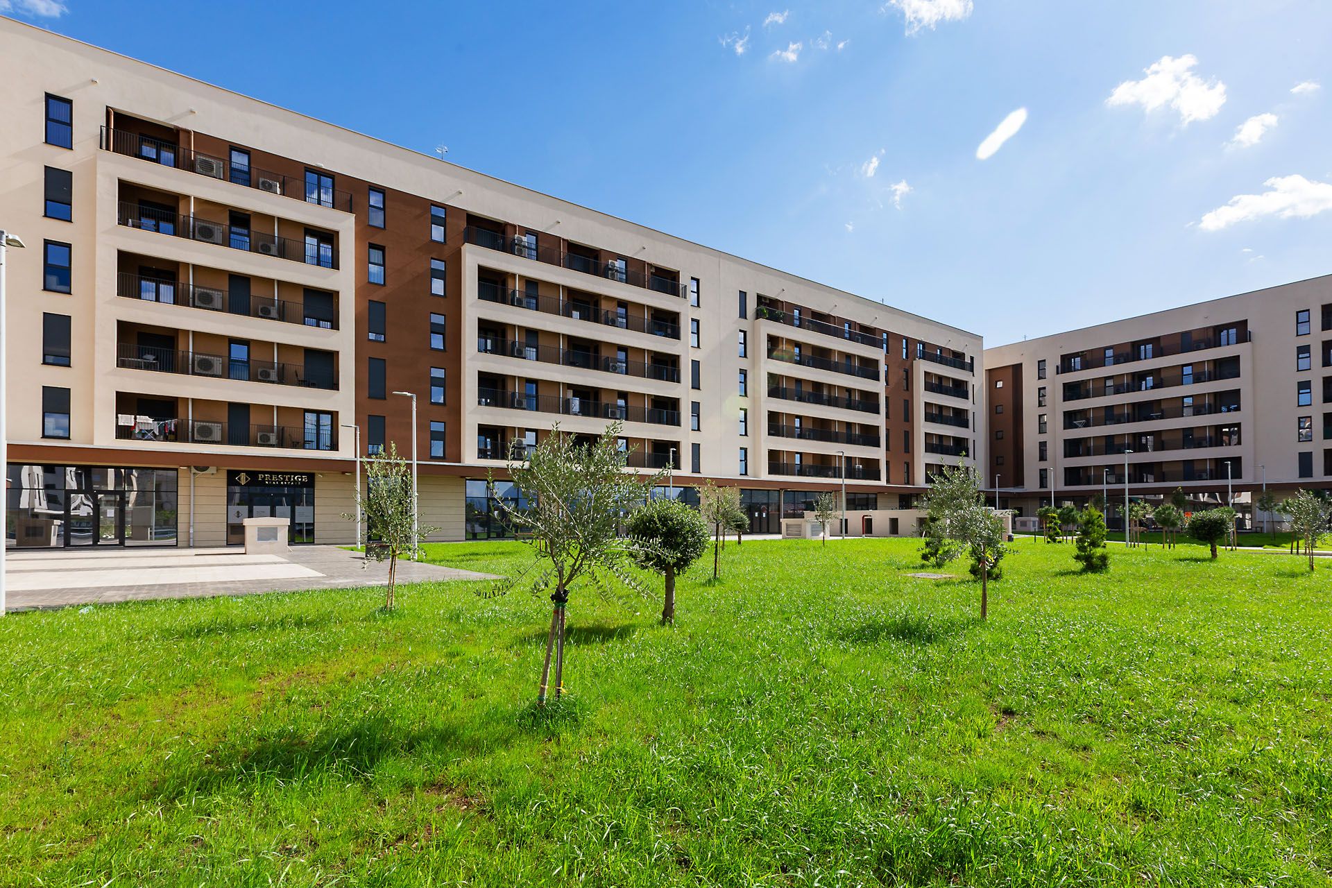 A multi-story residential building with balconies, a grassy courtyard, and a storefront.