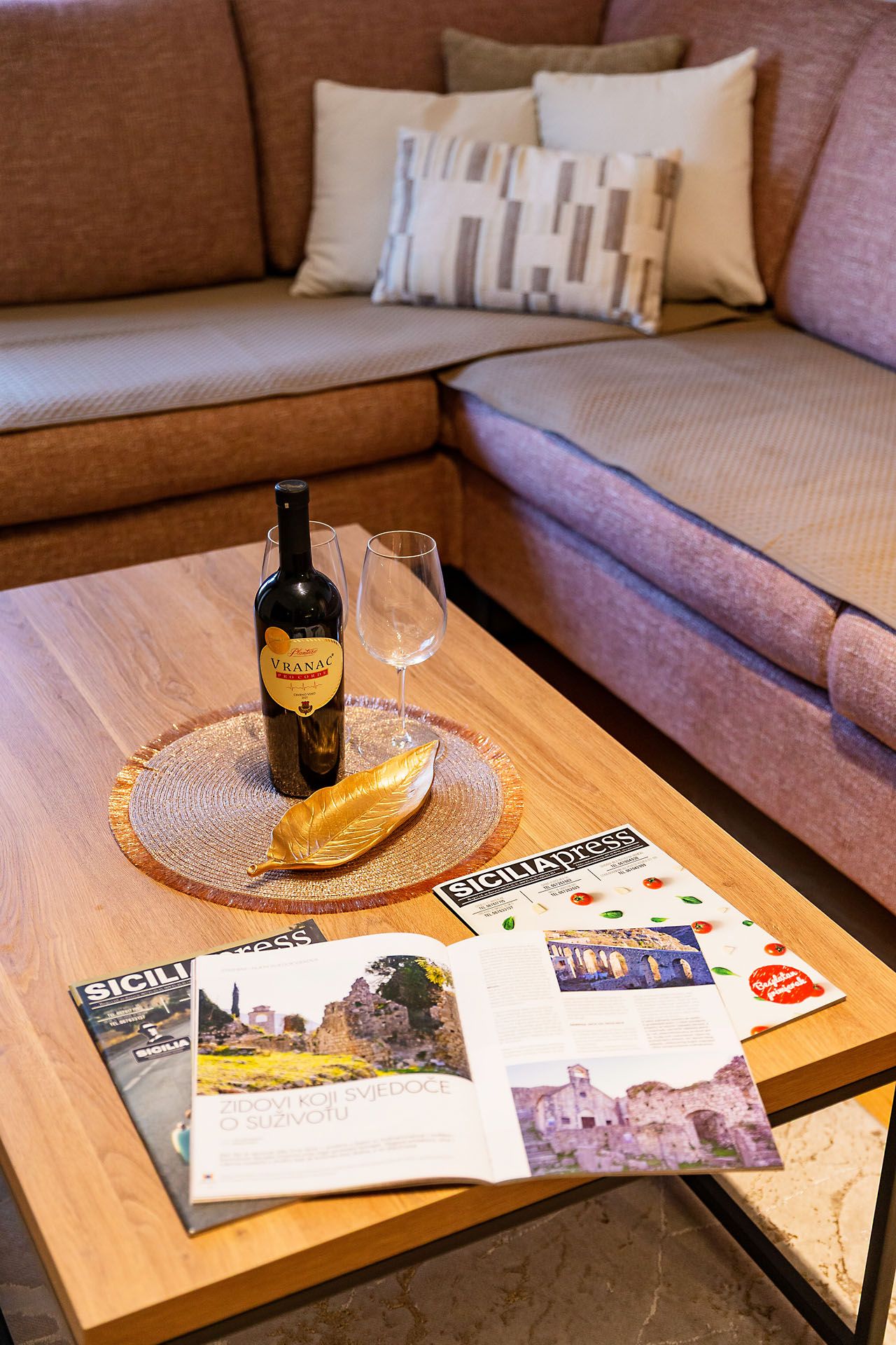 Une table basse en bois, avec une bouteille de vin, un verre et des magazines.