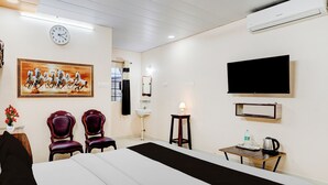 Quarto de hotel com cama, duas cadeiras, televisão, relógio e um quadro na parede.