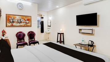 Una habitación de hotel con una cama, dos sillas, un televisor, un reloj y un cuadro en la pared.