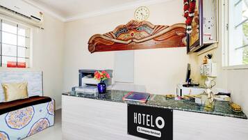 A hotel reception desk with a clock, a vase with flowers, and a sign indicating the hotel is company-serviced.