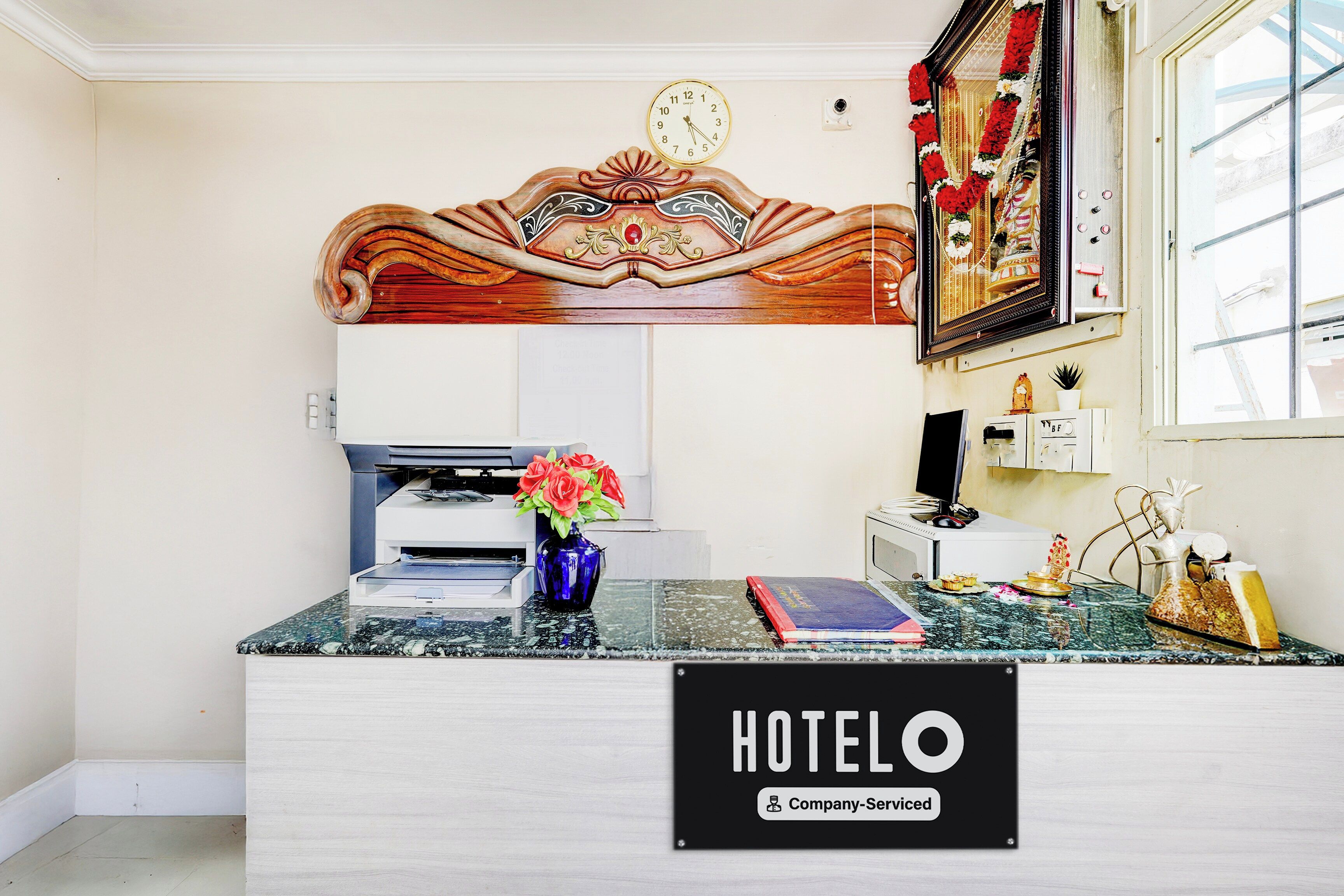 A hotel reception desk with a clock, a printer, and a vase with flowers.