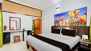 Quarto de hotel com uma cama, escrivaninha, cadeira, espelho e uma pintura de tulipas.