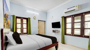 Quarto de hotel com cama, televisão de tela plana, relógio e janela com cortinas.