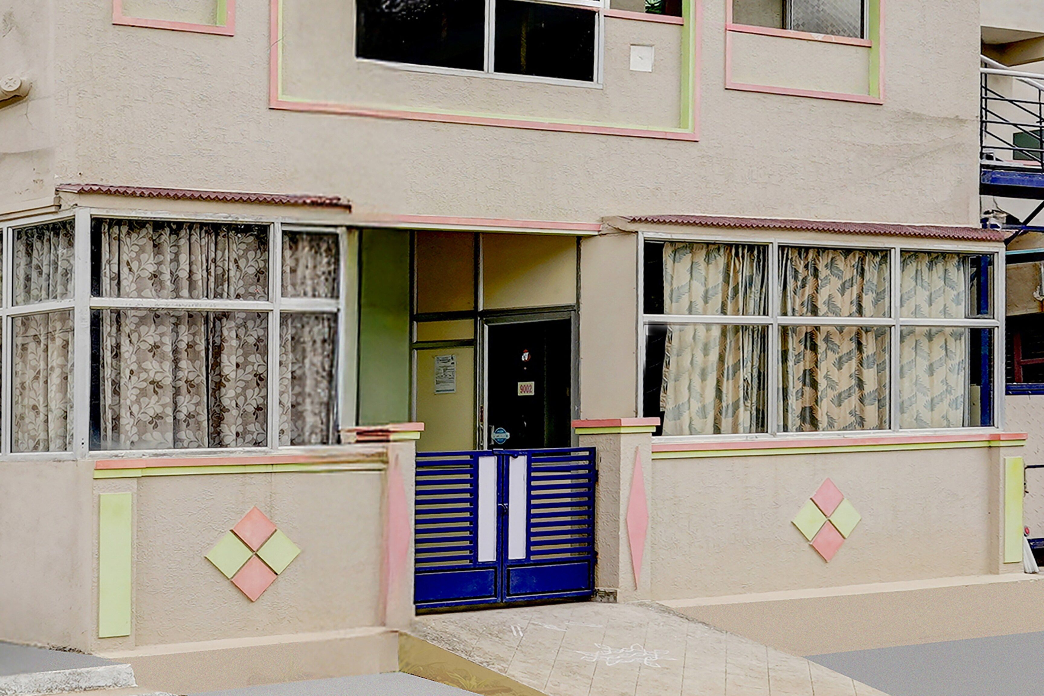 A two-story building with a flat facade, a central entrance, and a blue gate.