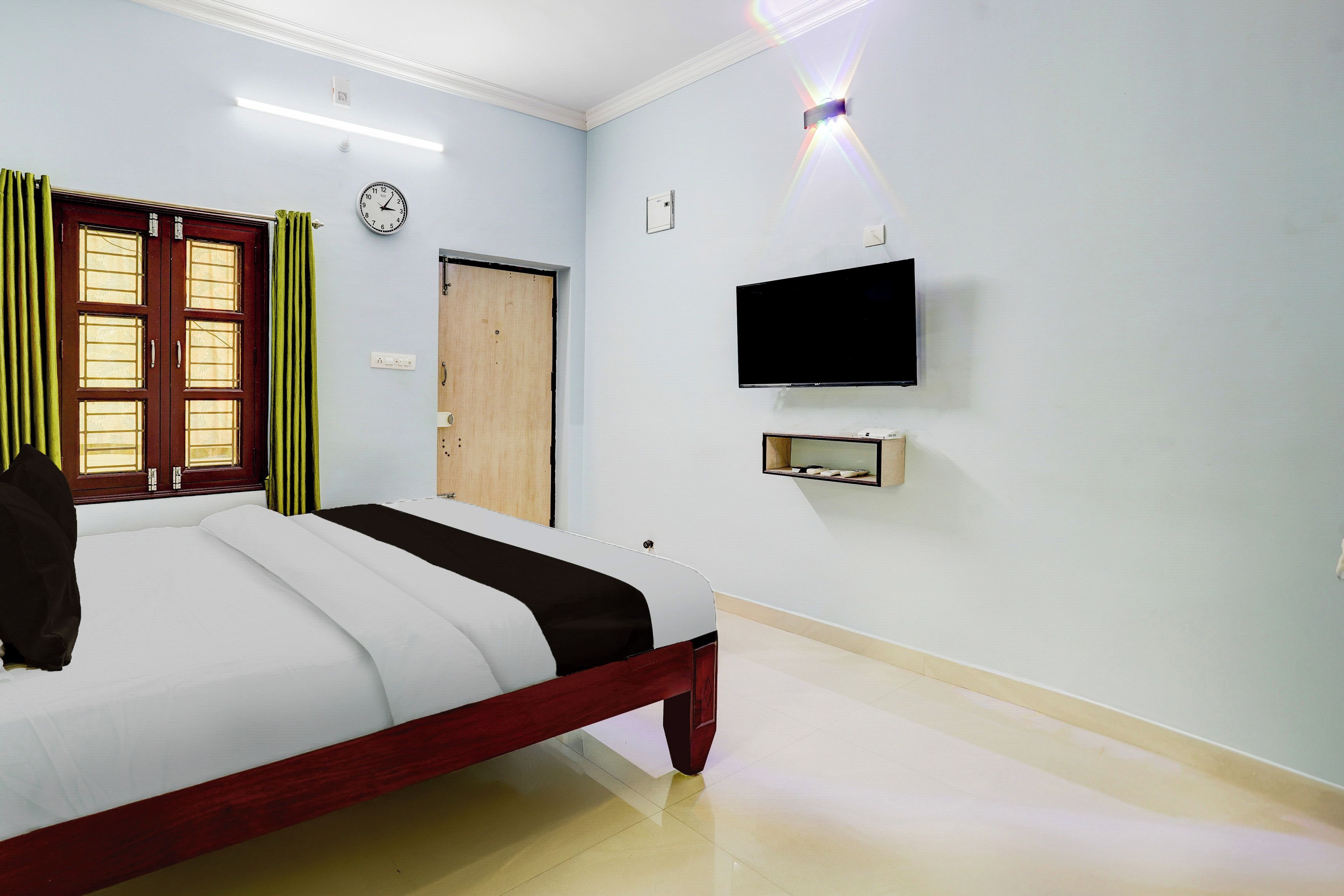 A hotel room with a bed, a television, a clock, and a door.