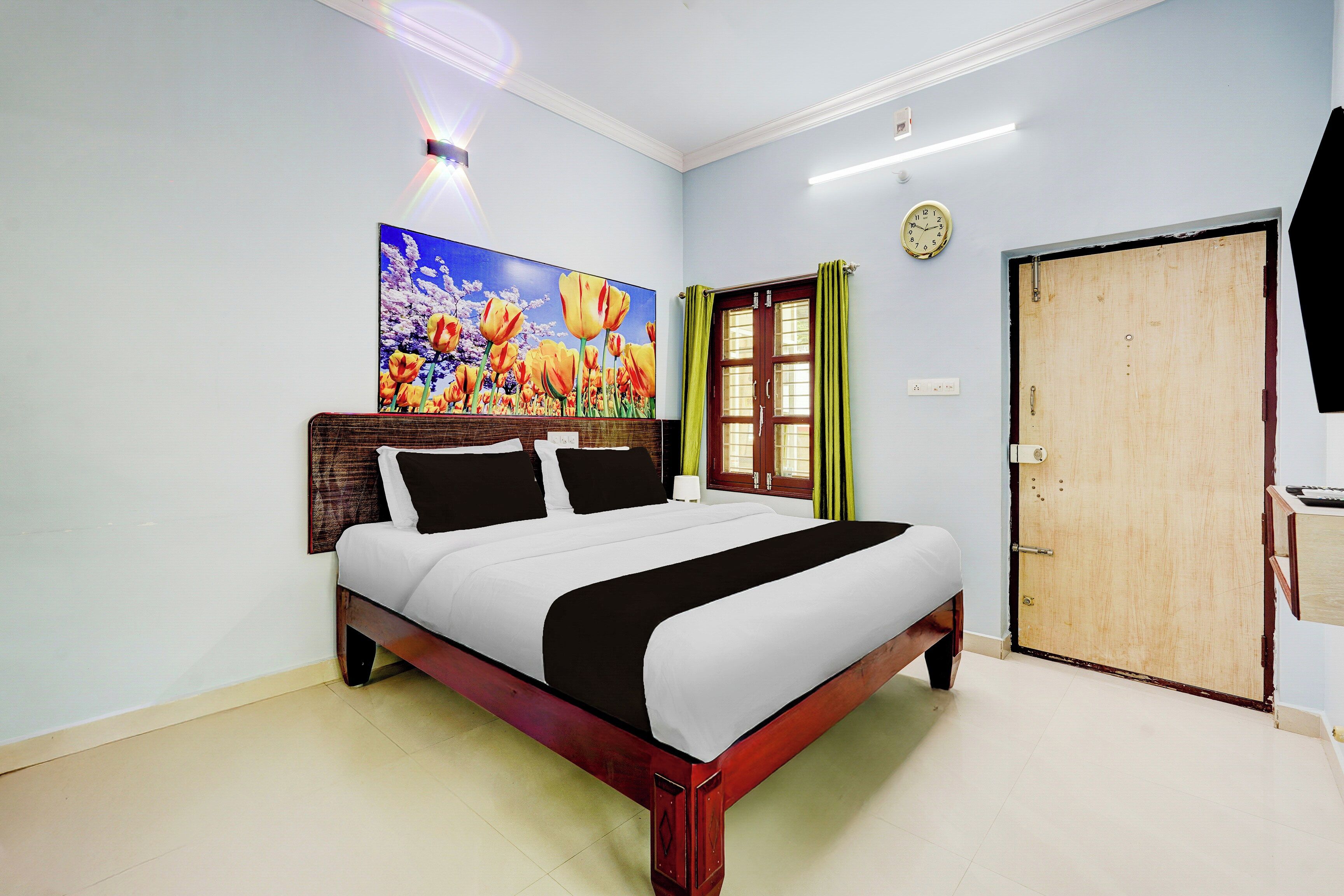Een hotelkamer met een bed, een schilderij, een klok en een deur.