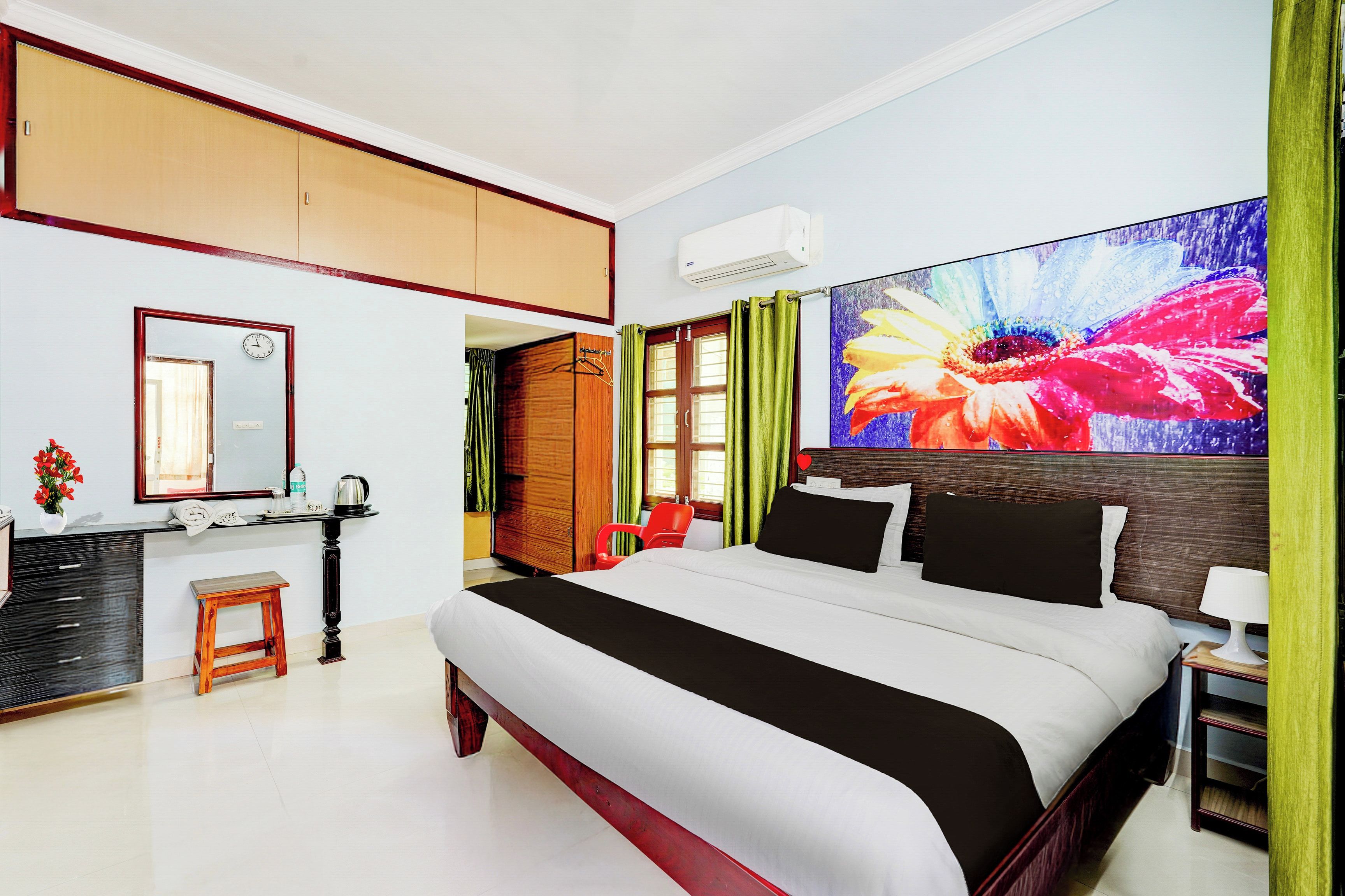 A hotel room with a large bed, a desk with a chair, a vanity with a mirror, and a large floral artwork on the wall.