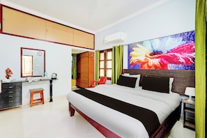 A hotel room with a large bed, a desk with a chair, a vanity with a mirror, and a large floral artwork on the wall. - Super Hotel O Chittoor Railway Station (Chittoor)
