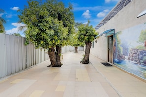 A corridor with tiled flooring, two trees, a white fence, and a mural on the wall.