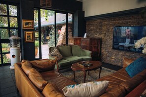 A living room with leather sofas, a coffee table, and a television mounted on a brick wall. - The Bohemian Guesthouse (Tzaneen)