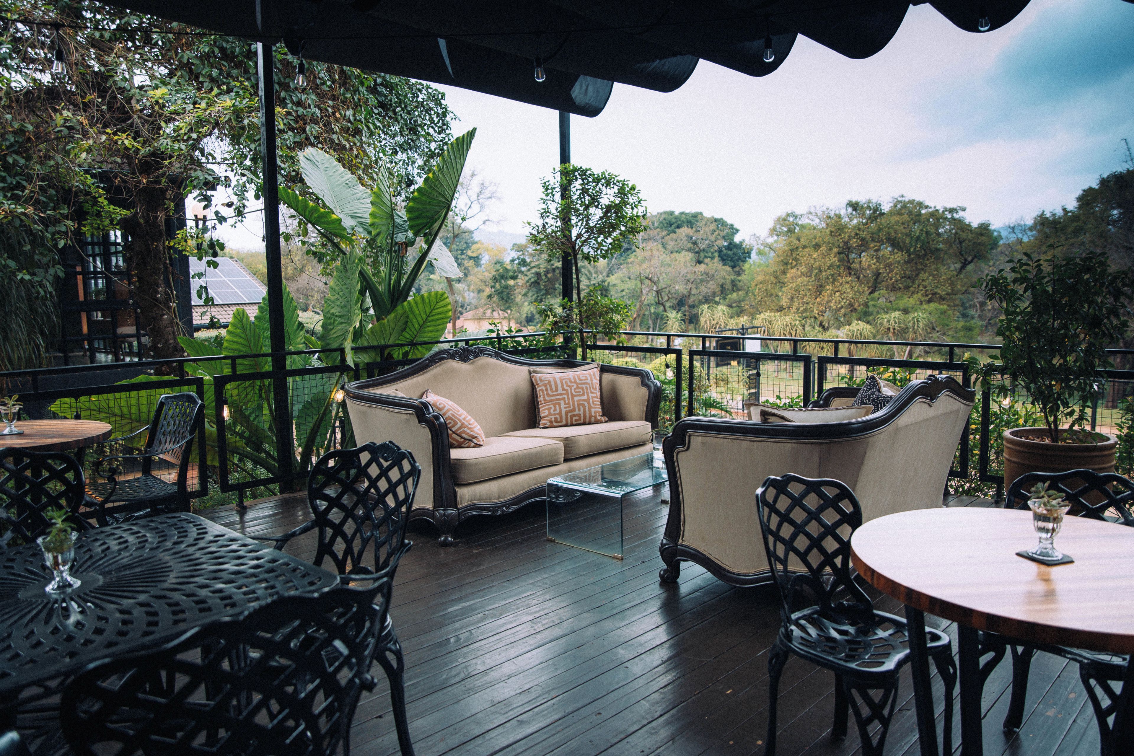 An outdoor seating area with a sofa, chairs, and tables, surrounded by a wooden deck and greenery.