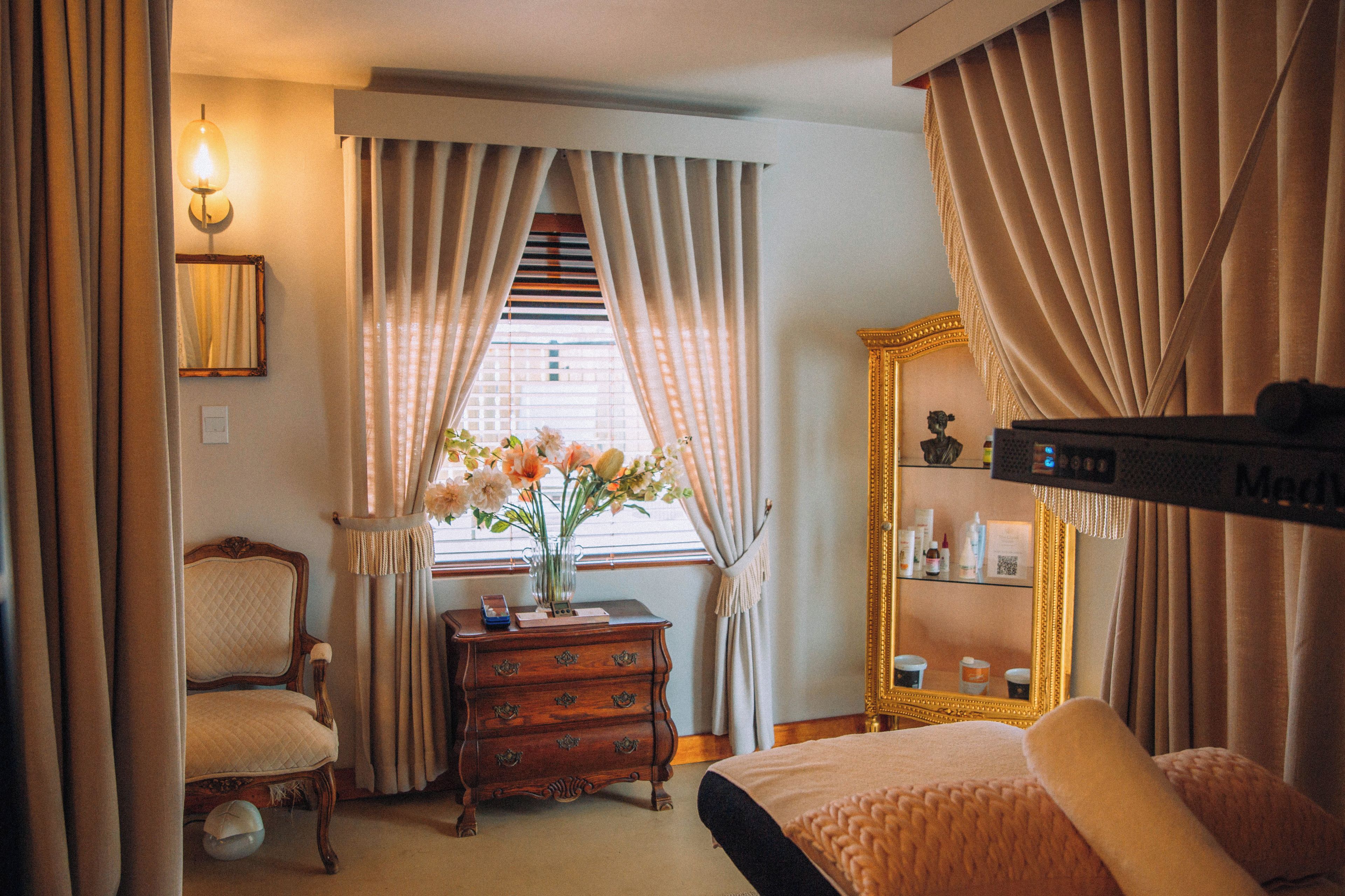 A bedroom with a bed, a dresser, a chair, a mirror, and a window with curtains.
