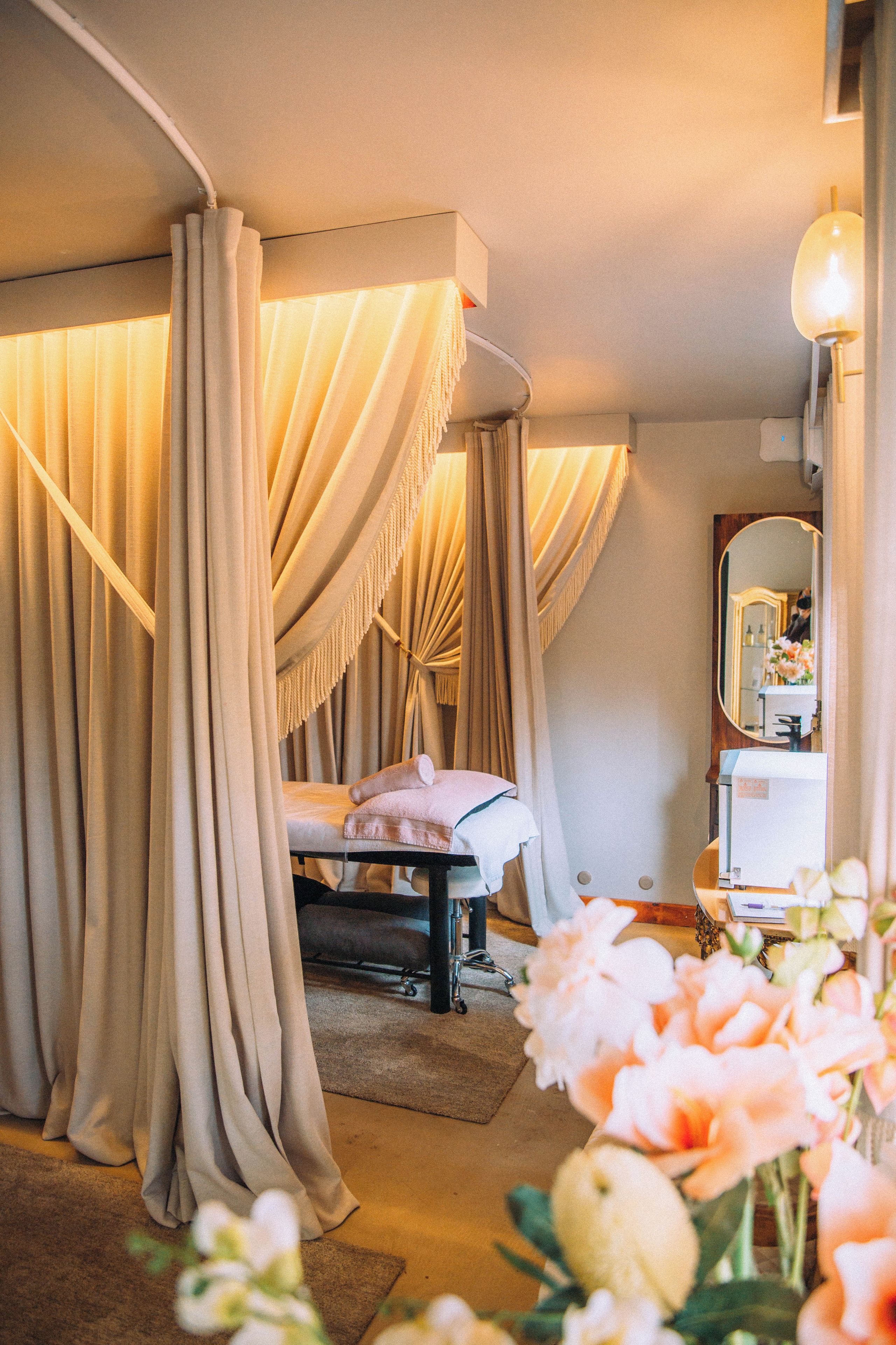 A room with a bed, curtains, a mirror, and a vase with flowers.