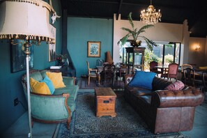 Un salón comedor de estilo tradicional con una pared verde, una araña y varios asientos, incluyendo un sillón verde, un sofá de cuero marrón y una mesa de centro de madera.