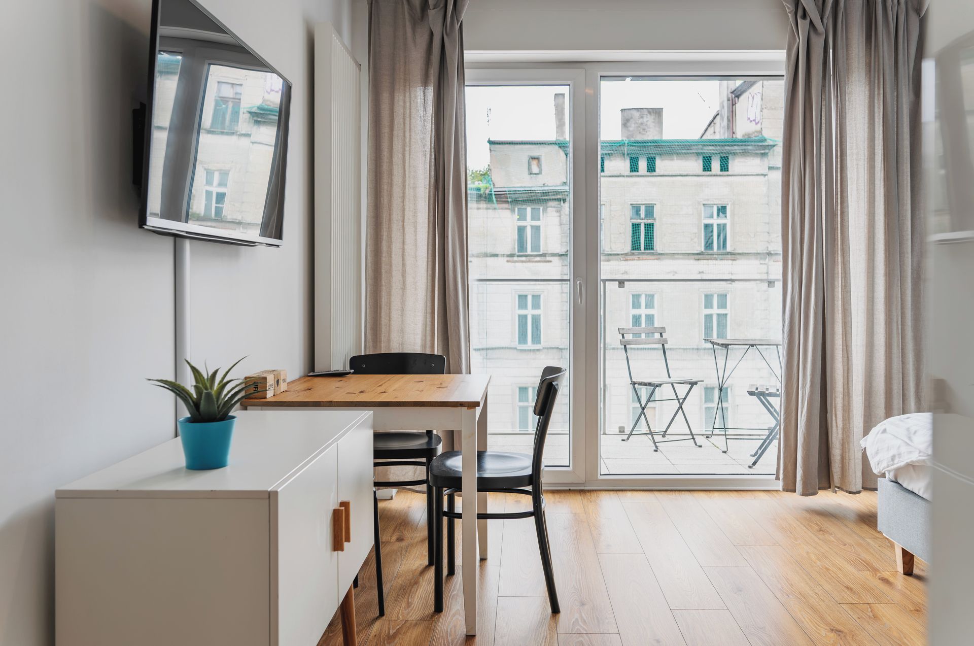 A modern apartment with a wooden dining table, a black chair, a white cabinet, and a potted plant.