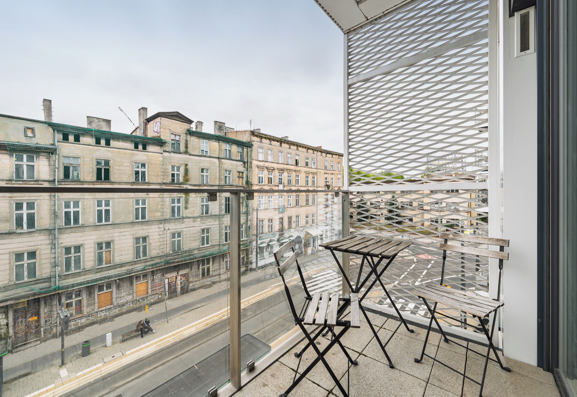 A balcony with a view of old buildings, a wooden table, and a metal chair.