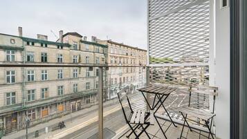 A balcony with a view of old buildings, a wooden table, and a metal chair.