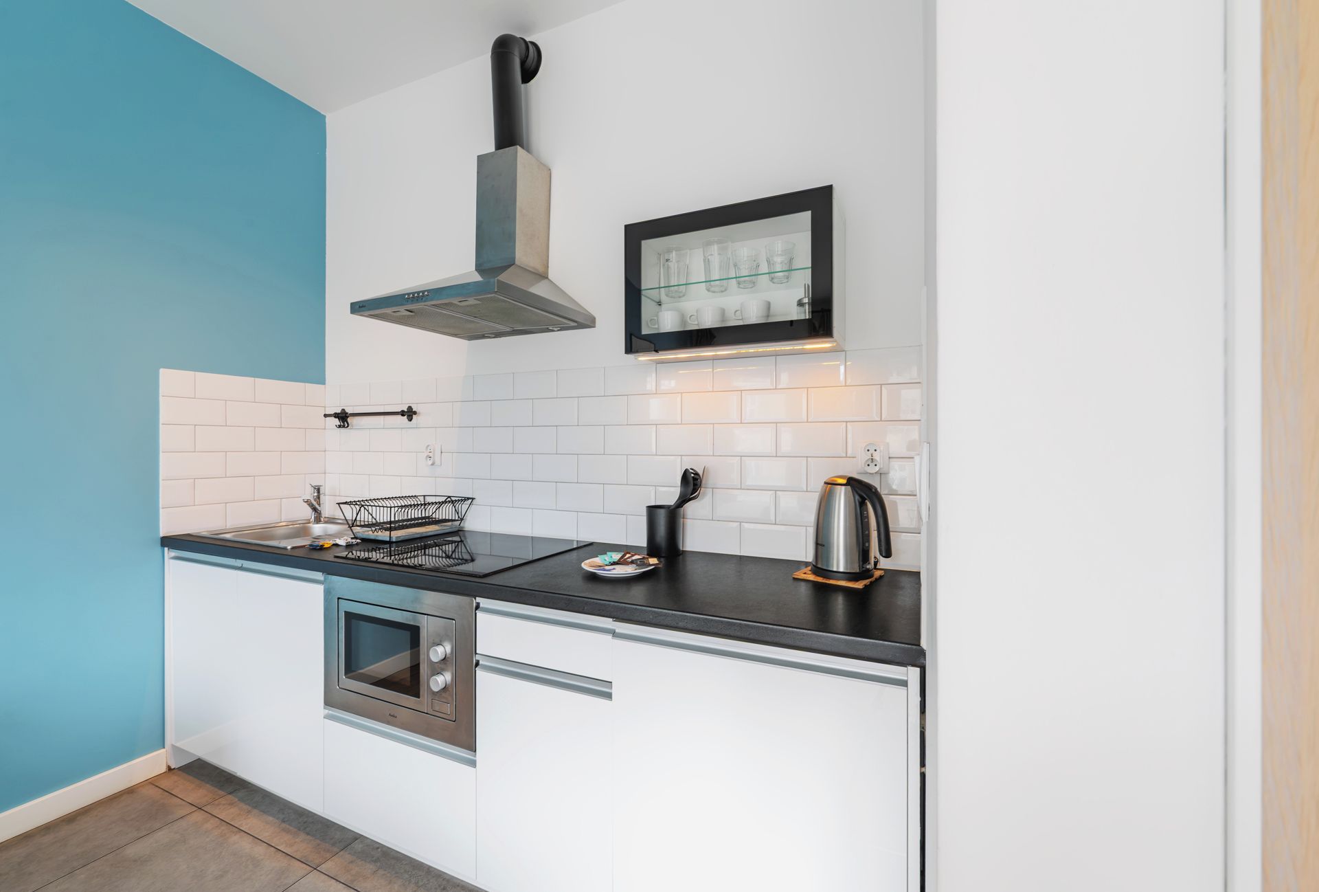 A compact kitchen with white cabinetry, a stainless steel oven, a kettle, and a coffee maker on the countertop.