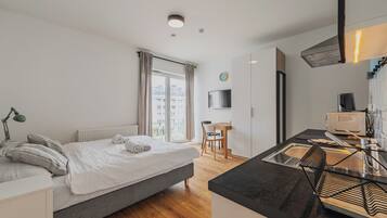 Una habitación de hotel moderna con cama, escritorio, silla, televisión y kitchenette.