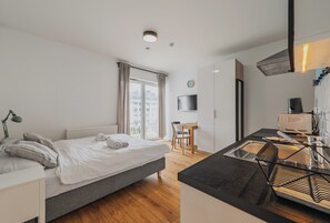 Una habitación de hotel moderna con cama, escritorio, silla, televisión y kitchenette.
