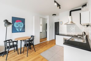 Una cocina moderna con encimera negra, pileta de acero inoxidable y campana extractora. Hay un comedor con mesa y sillas, y una lámpara de pie negra.