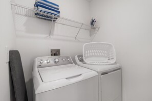 A laundry area with a washing machine, a dryer, a shelf with towels, and a laundry basket. - 8863 Cabot Cliffs Dr Unit 101 (Davenport)