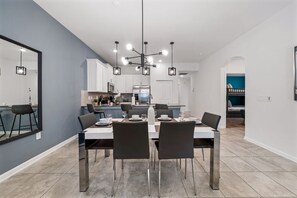 A modern dining area with a central table, chairs, and a kitchen in the background. - 8863 Cabot Cliffs Dr Unit 101 (Davenport)
