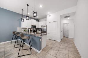 A modern kitchen with white cabinets, a stainless steel refrigerator, and a bar area with stools. - 8863 Cabot Cliffs Dr Unit 101 (Davenport)