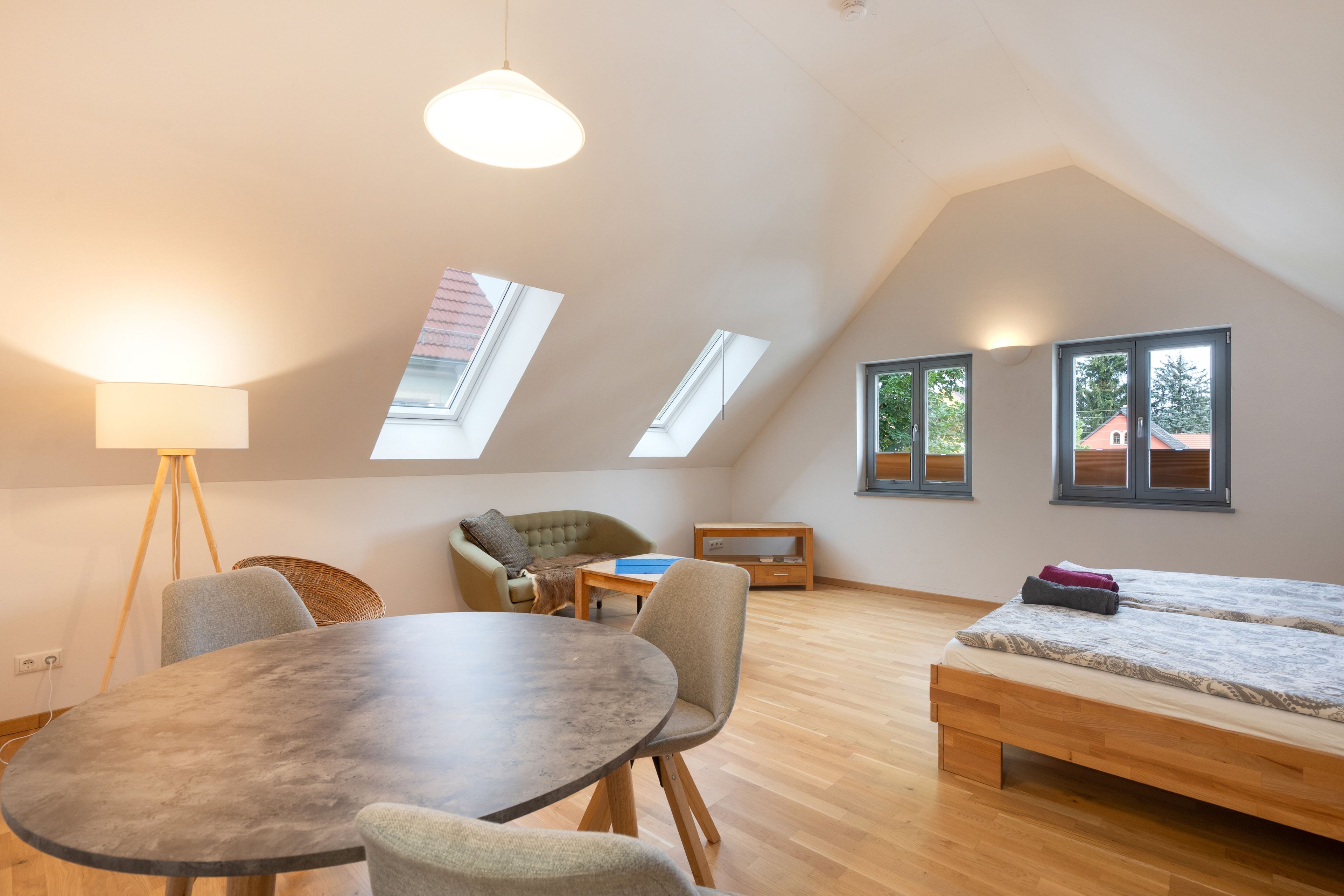 A room with a round table, two chairs, a sofa, a bed, and skylights.
