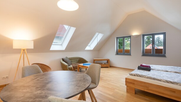 Ein Zimmer mit einem runden Tisch, zwei Stühlen, einem Sofa, einem Bett und Dachfenstern.