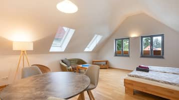 A room with a round table, two chairs, a sofa, a bed, and skylights.