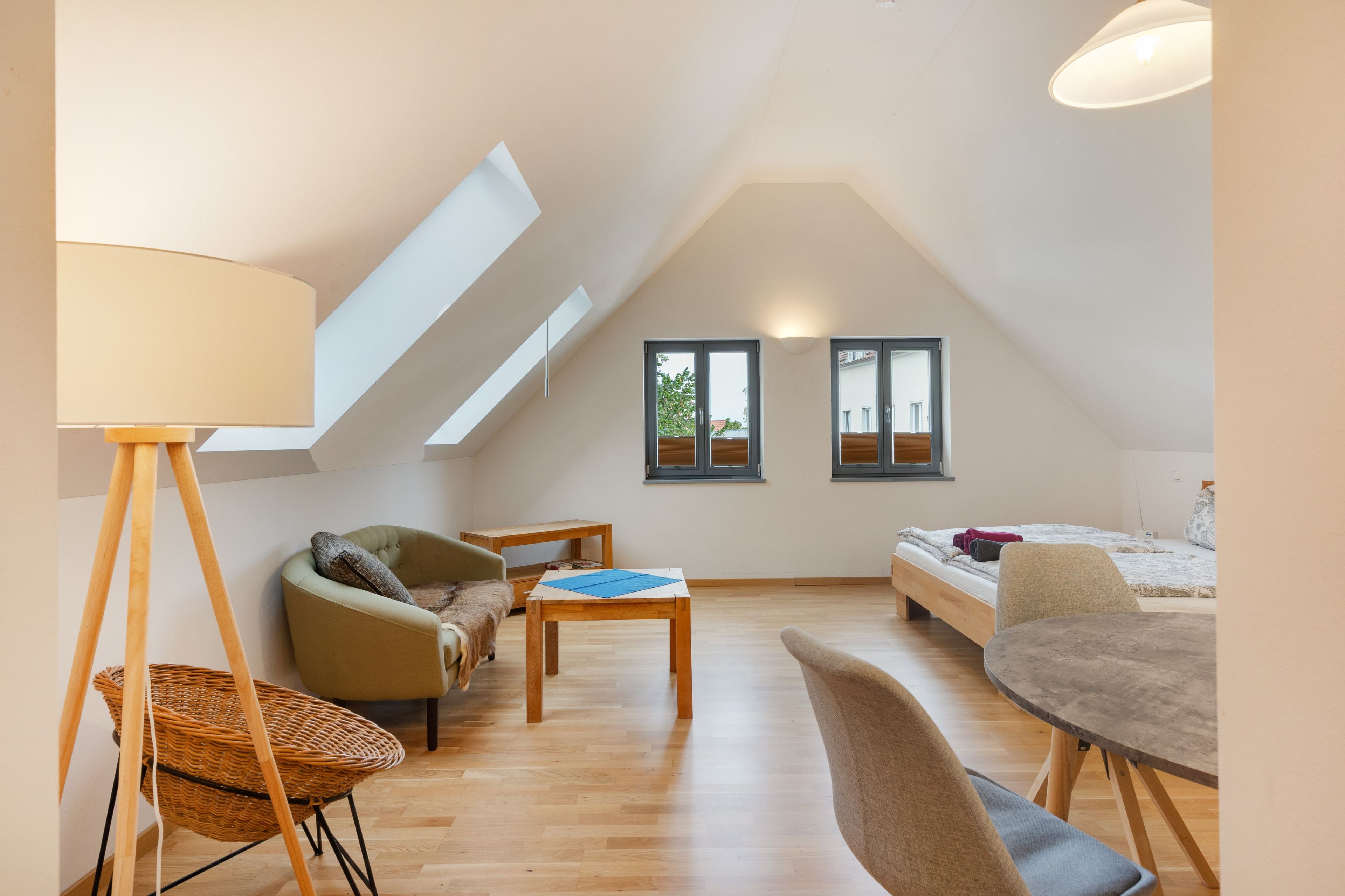 Ein modernes Schlafzimmer im Loft-Stil mit schrägem Dach, einem Bett, einer Sitzecke mit Tisch und einem großen Fenster.