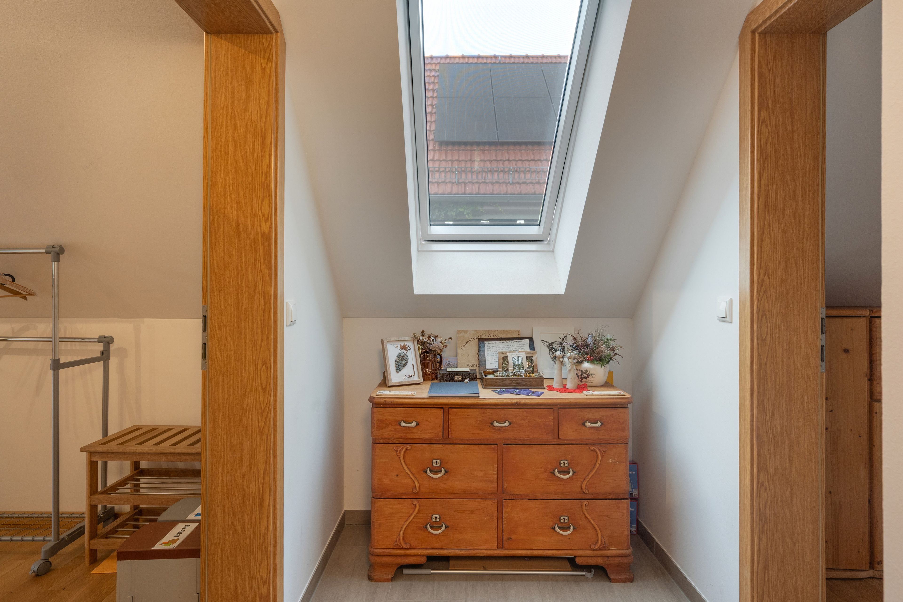 A room with a skylight, wooden dresser, and a metal rack.