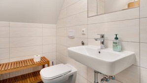 Ein Badezimmer mit einem weißen Waschbecken, einer Toilette und einer hölzernen Sitzbank.