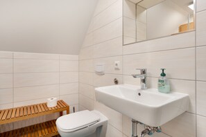 A bathroom with a white sink, a toilet, and a wooden bench. - Apartment 'Zieglinde-Ziegenhof' (Radebeul)