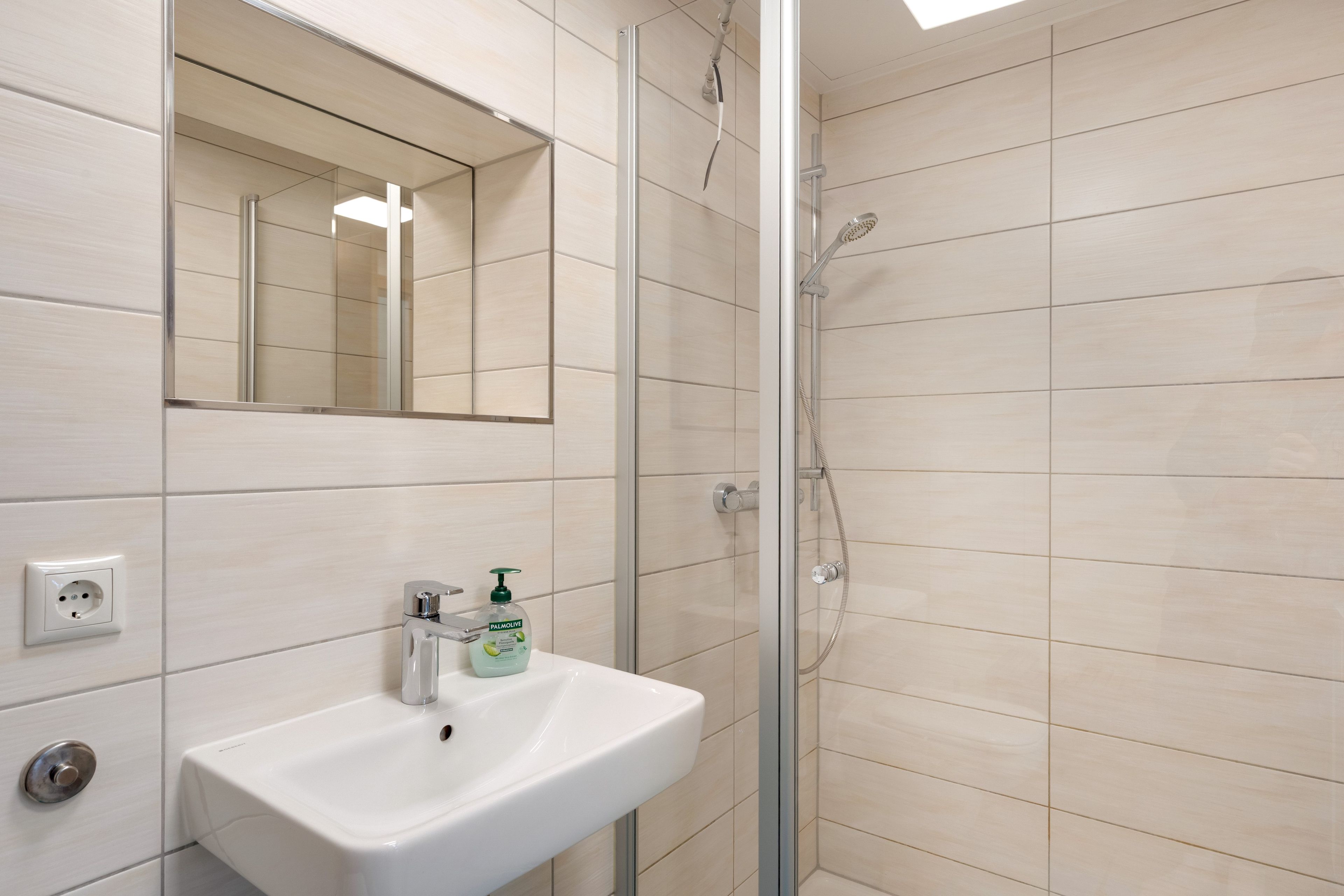 Ein Badezimmer mit einem weißen Waschbecken, einem Spiegel und einer Dusche.