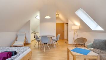 A modern loft apartment with a dining area, a sofa, a bed, and a skylight.