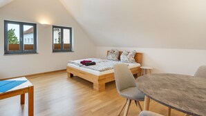 Ein Schlafzimmer mit schrägem Dach, einem hölzernen Bett, einem kleinen Tisch und einem Stuhl.