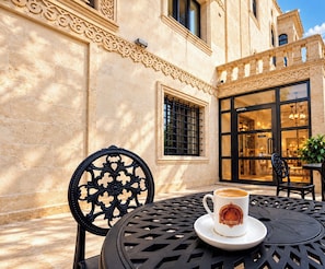 An outdoor seating area with a table and chairs, a cup of coffee, and a building entrance with decorative elements.