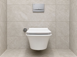 A modern bathroom with a toilet, a wall-mounted flush valve, and a control panel.