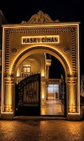 Uma entrada imponente com um arco ornamentado com a inscrição 'KASR'I CIHAN', dando acesso à área de recepção.
