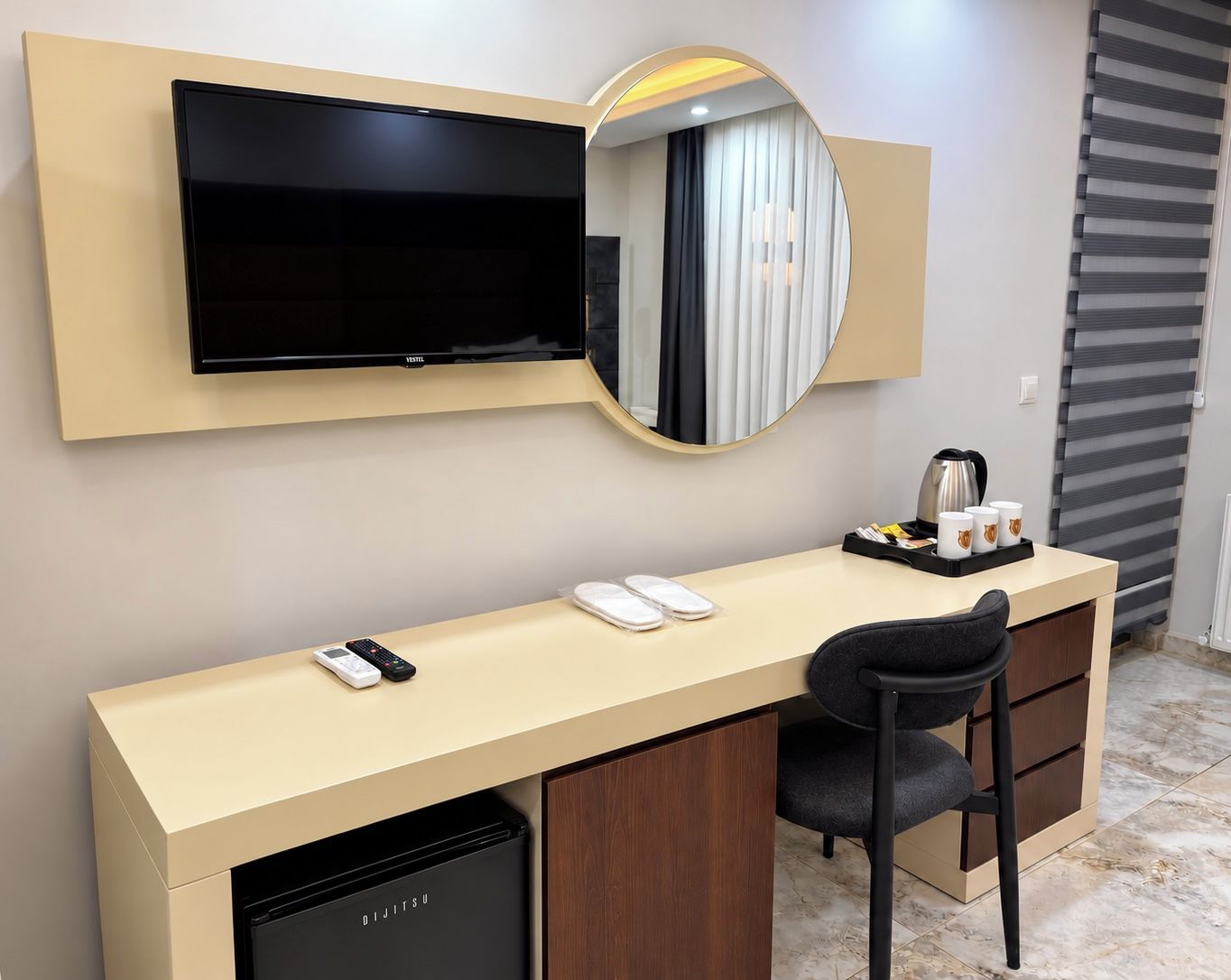 Ett hotellrum med en minibar, en platt-TV, ett skrivbord med en stol och en kaffebryggare.