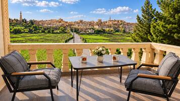 A balcony with two chairs and a table, overlooking a terraced landscape and a distant cityscape.