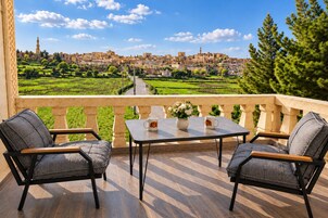 Un balcón con dos sillas y una mesa, con vistas a un paisaje escalonado y un horizonte urbano distante.